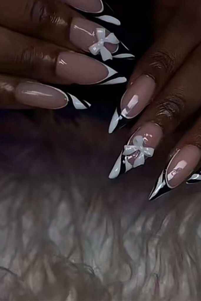 moderate nude nails with white and black designed tips and bow tie design