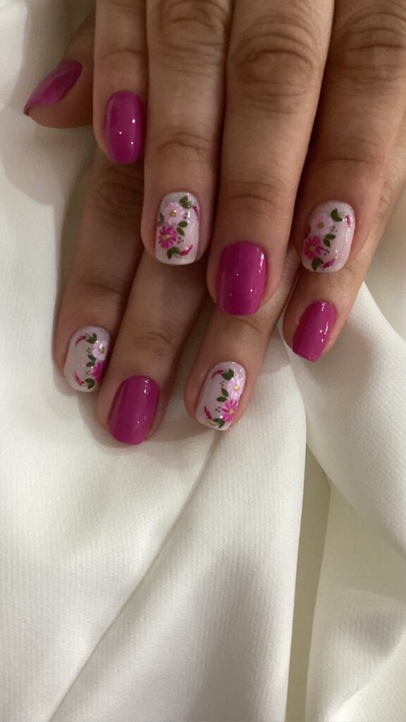 A magenta color nail with a floral design on the second and fourth finger nails.
