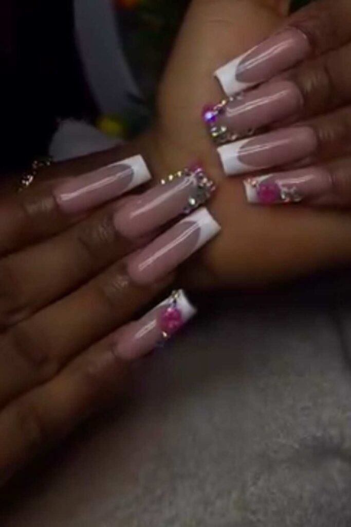 A picture of white modern French tips nails with some shiny stone design on the tip of the mid finger.
