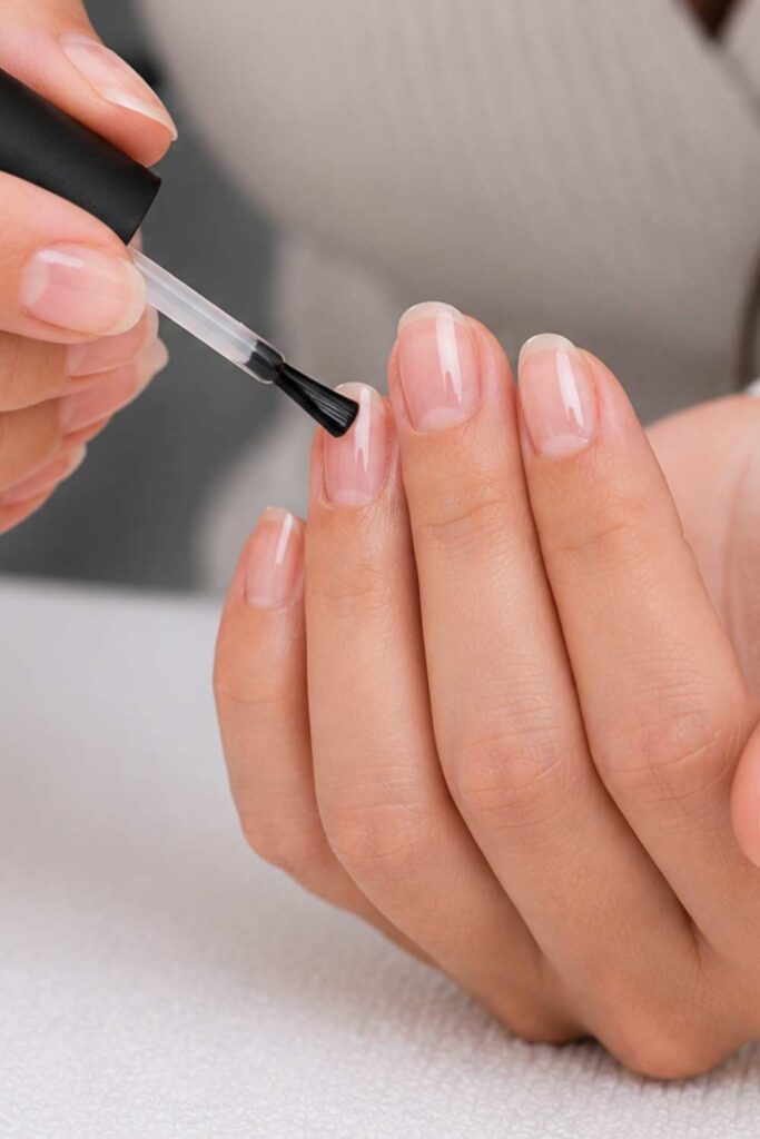 A picture of a lady applying a base coat on the nails