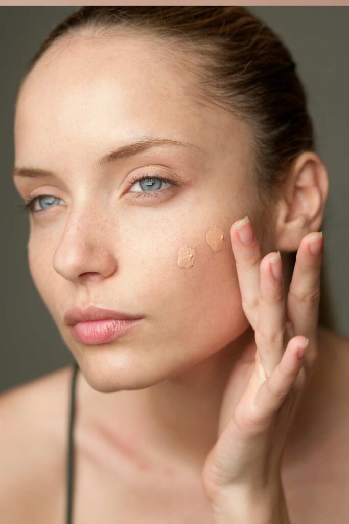 A lady using her finger to apply foundation on her face.